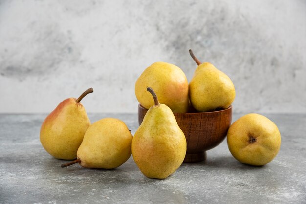 Mazzo di bio pere fresche in una ciotola di legno su una superficie di marmo.