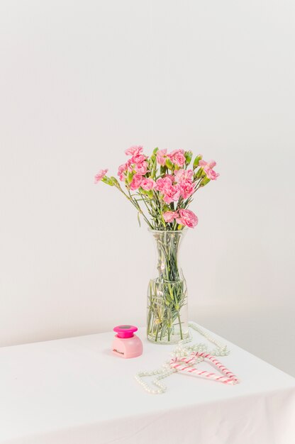 Mazzo di fiori in vaso vicino a bastoncini di zucchero, scatola e perline sul tavolo