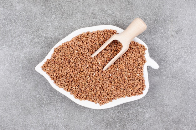 Mazzo di grano saraceno crudo sulla zolla bianca con il cucchiaio di legno