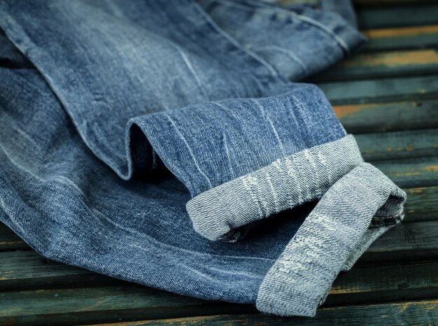 mazzo di jeans su uno sfondo di legno cosparso di jeans, close-up, vestiti alla moda