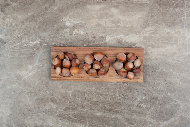 Mazzo di nocciole nel piatto di legno sulla parete di marmo.