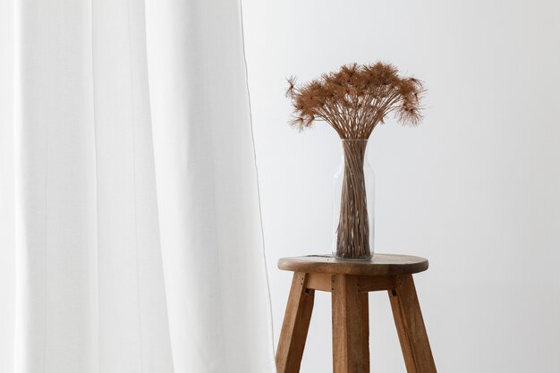 Mazzo di papiro secco pianta in un vaso di vetro su uno sgabello di legno da una tenda bianca