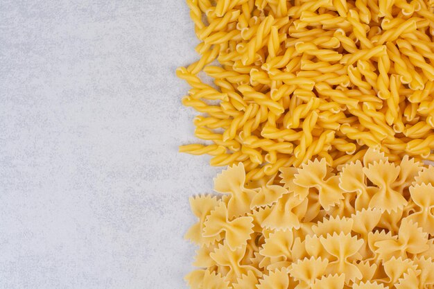 Mazzo di pasta cruda a spirale e farfalle su sfondo marmo.