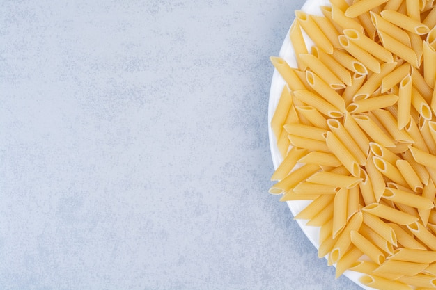 Mazzo di pasta di penne gialla sulla zolla bianca