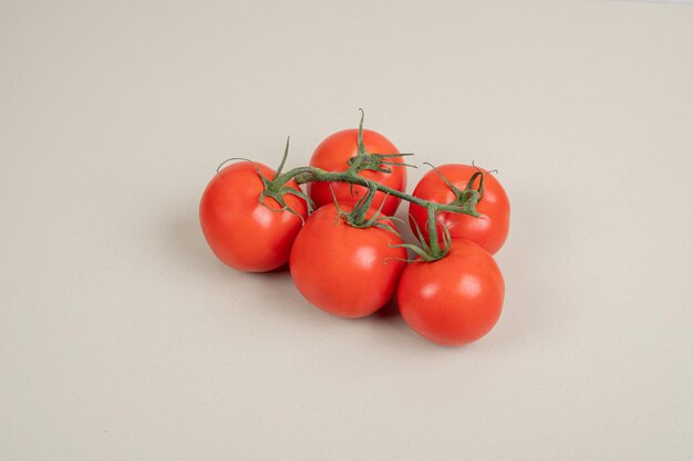 Mazzo di pomodori freschi e rossi con steli verdi sul tavolo bianco.