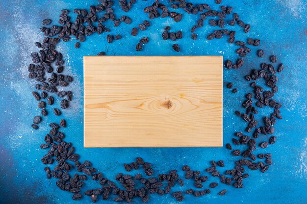 Mazzo di uvetta nera e tavola di legno sul tavolo blu.