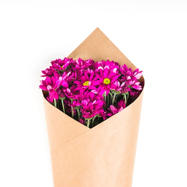 Mazzo rosa del fiore avvolto con carta marrone contro fondo bianco