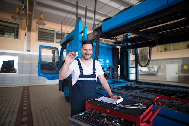 Meccanici di camion di mezza età esperti che tengono parti e strumenti in officina vicino al camion