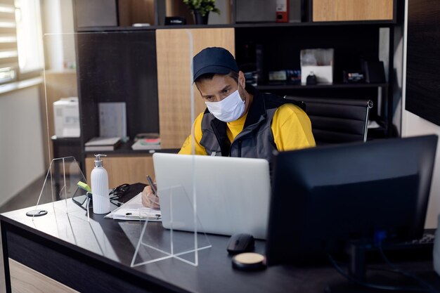 Meccanico automatico che utilizza il laptop mentre esamina le scartoffie in ufficio durante la pandemia di COVID19