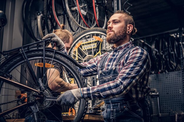 Meccanico barbuto testa rossa che fissa il deragliatore posteriore da una bicicletta in un'officina.