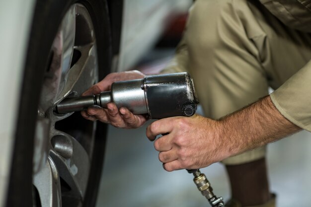 Meccanico che ripara una ruota di automobile con la chiave pneumatica