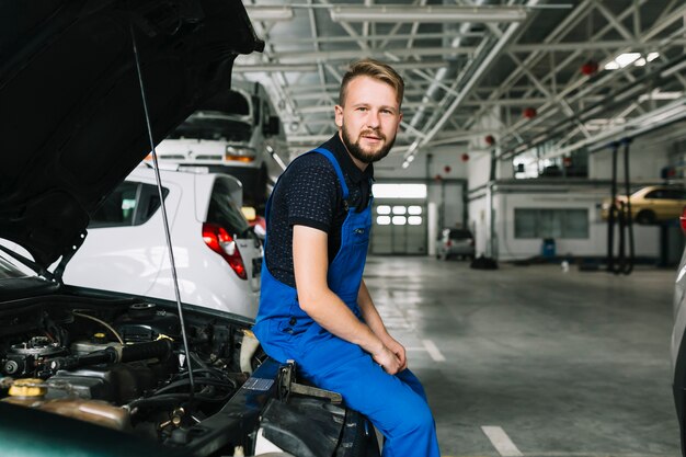 Meccanico che si siede sull&#39;automobile all&#39;officina