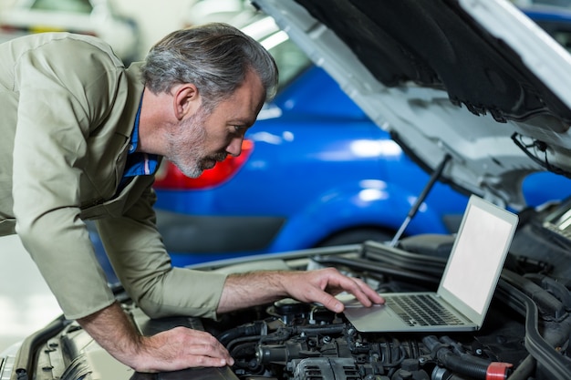 Meccanico con laptop, mentre la manutenzione del motore auto