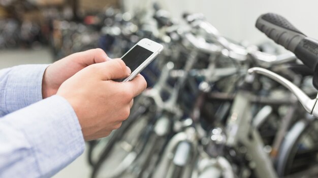 Meccanico della bicicletta che utilizza cellulare nel negozio