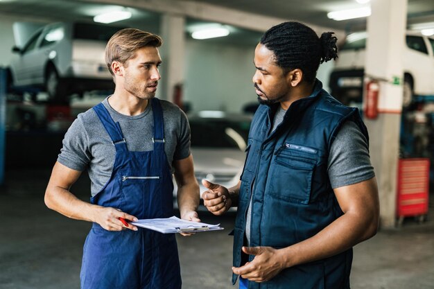 Meccanico di automobile afroamericano e il suo collega che comunicano nell'officina riparazioni auto
