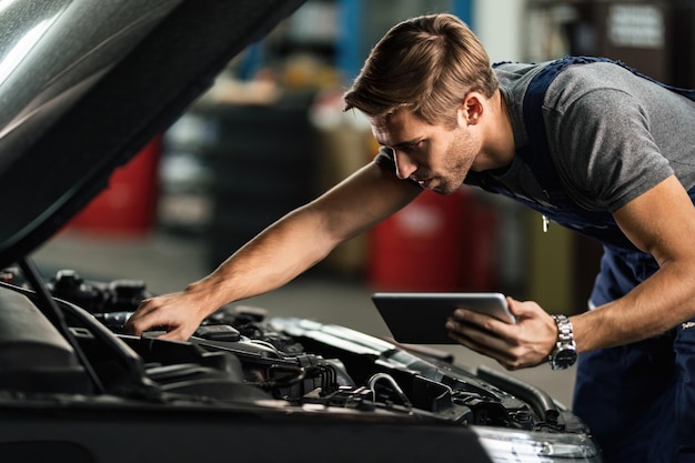 Meccanico di automobile che esamina il malfunzionamento del motore durante l'utilizzo del touchpad nell'officina riparazioni auto