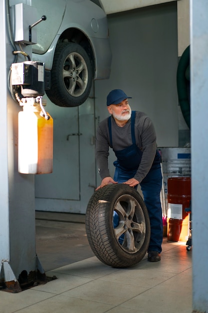 Meccanico di automobile maschio che maneggia la ruota nell'officina di riparazione auto