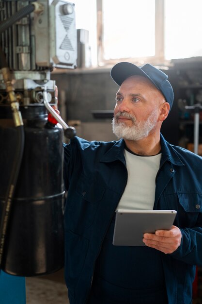 Meccanico di automobile maschio che utilizza il dispositivo della compressa nell'officina di riparazione dell'automobile