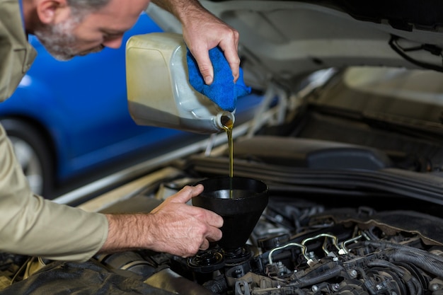 Meccanico di olio versando in motore di automobile