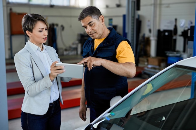 Meccanico e manager femminile che collaborano mentre lavorano al touchpad nell'officina di riparazioni auto