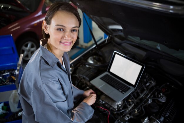 Meccanico femminile esaminando motore di automobile con l&#39;aiuto del computer portatile