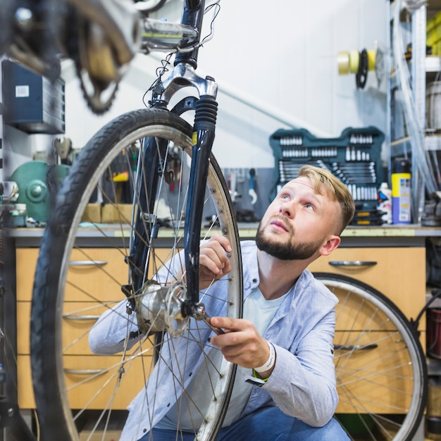 Meccanico maschio della bicicletta che ripara la gomma della bicicletta in negozio