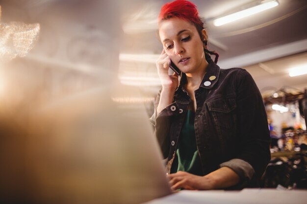 Meccanico parlando al telefono cellulare mentre si utilizza laptop