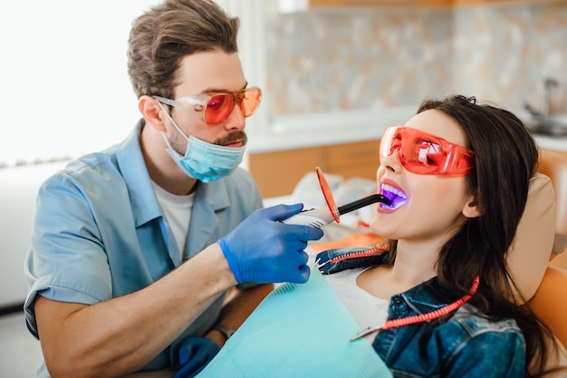 Medicina, odontoiatria e concetto di assistenza sanitaria, dentista che utilizza lampada UV di polimerizzazione dentale sui denti del paziente.