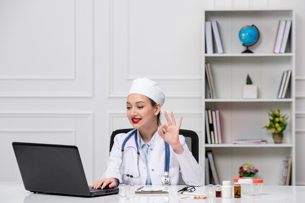 Medico adorabile carino medico in camice bianco e cappello con computer che parla videochiamata al cliente