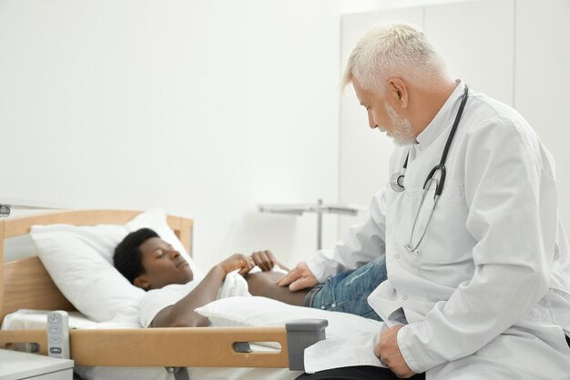 Medico anziano che esamina la pancia del paziente africano