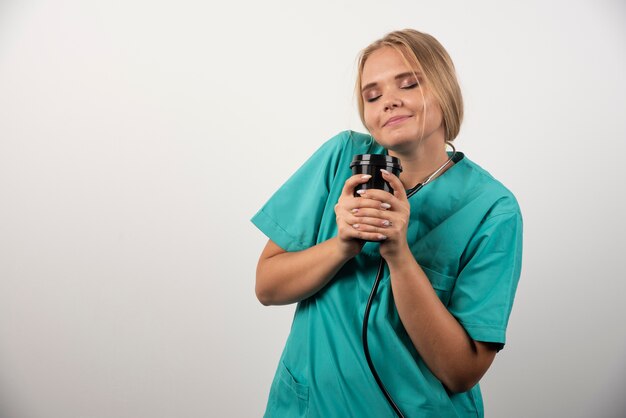 Medico biondo che posa con la tazza di caffè sulla parete bianca.