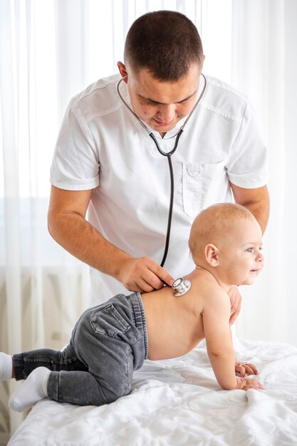Medico che ascolta piccolo bambino sveglio con lo stetoscopio