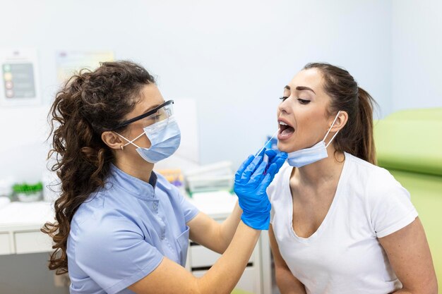 Medico che esegue il test del tampone faringeo da una paziente di sesso femminile L'operatore medico è in abbigliamento protettivo da lavoro Sono in ospedale durante l'epidemia