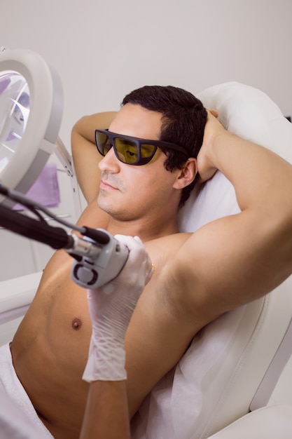 Medico che esegue la depilazione laser sulla pelle del paziente maschio