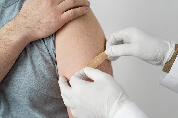 Medico che mette la fasciatura sul braccio del paziente maschio dopo l'iniezione del vaccino