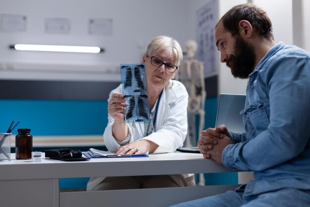 Medico che spiega la diagnosi radiografica all'uomo con la malattia durante la visita di controllo. Specialista che mostra i risultati della scansione a raggi X al paziente, discutendo sull'assistenza sanitaria e sul trattamento medico