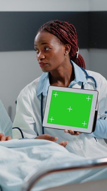 Medico che tiene tablet digitale con schermo verde orizzontale, che mostra la tecnologia al paziente. Medico e persona che guarda il modello di mockup isolato e lo sfondo sul display della chiave cromatica