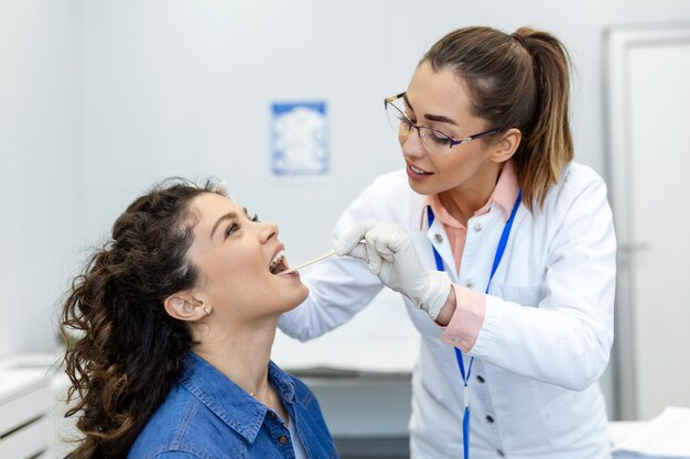 Medico che utilizza la spatola di ispezione per esaminare la gola del paziente Medico ORL che esegue l'esame della gola di una paziente donna che ha aperto la bocca al controllo della gola