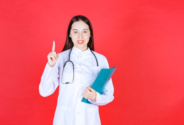 Medico con uno stetoscopio che tiene la storia del paziente e alza la mano per fare una domanda.