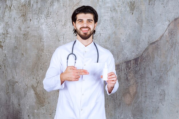 Medico con uno stetoscopio che tiene un tubo bianco di spray disinfettante per le mani