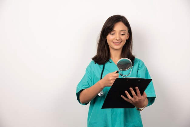 Medico della donna che esamina appunti con la lente d'ingrandimento su priorità bassa bianca. Foto di alta qualità