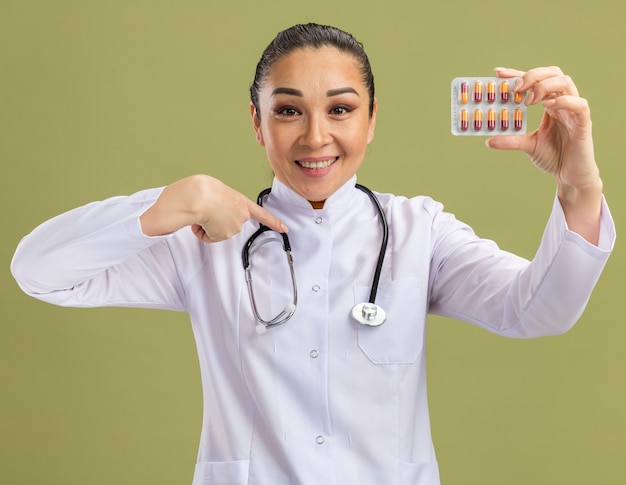 Medico della giovane donna che tiene blister con le pillole che puntano con il dito indice sorridendo fiducioso