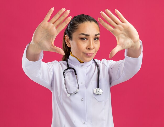 Medico della giovane donna con il fronte serio che fa il gesto di arresto con le mani aperte