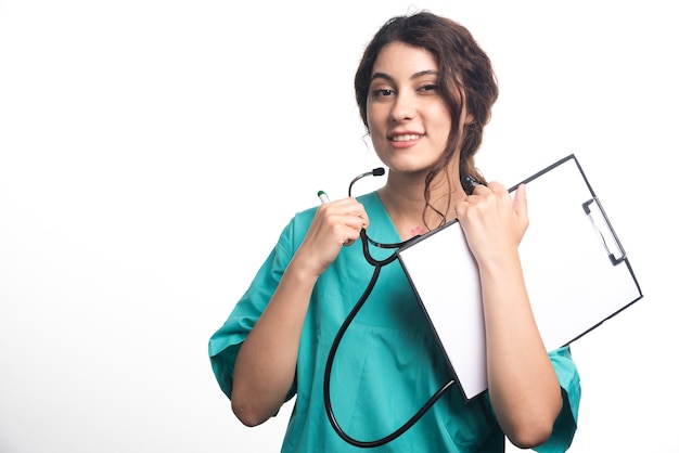 Medico della giovane donna con lo stetoscopio che tiene appunti in uniforme su priorità bassa bianca. Foto di alta qualità