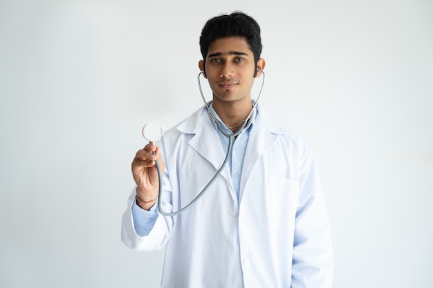 Medico di famiglia maschio serio che utilizza stetoscopio e che guarda l&#39;obbiettivo.