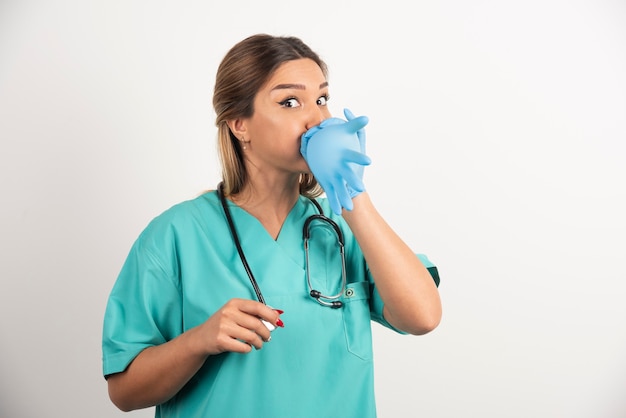 Medico di giovane donna che indossa guanti in lattice e scrub su sfondo bianco.