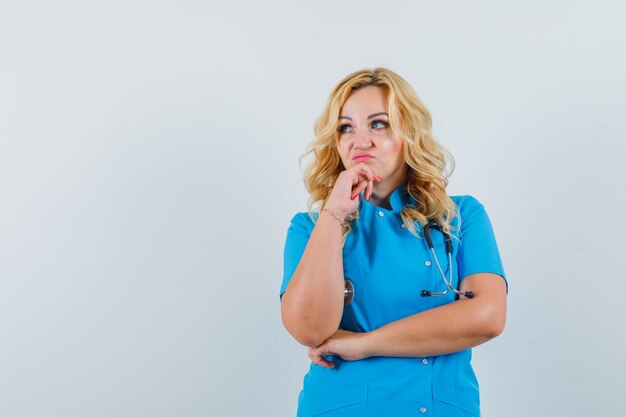 Medico donna che guarda lontano in uniforme blu e cerca pensieroso spazio per il testo