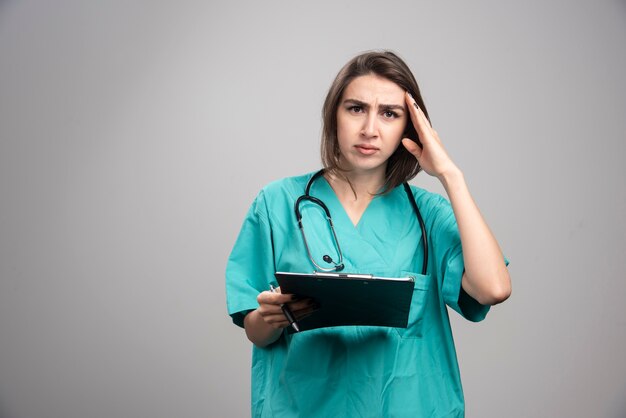 Medico donna che ha mal di testa sul muro grigio.