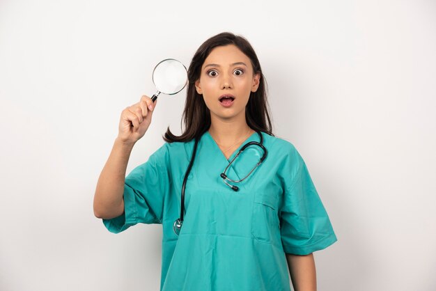 Medico donna con lente d'ingrandimento su sfondo bianco. Foto di alta qualità