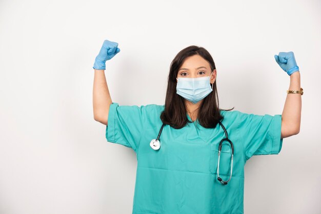 Medico donna con maschera che mostra i suoi muscoli su sfondo bianco. Foto di alta qualità